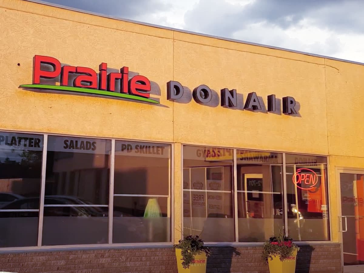 Prairie Donair storefront at dusk with the red and lime sign lit up